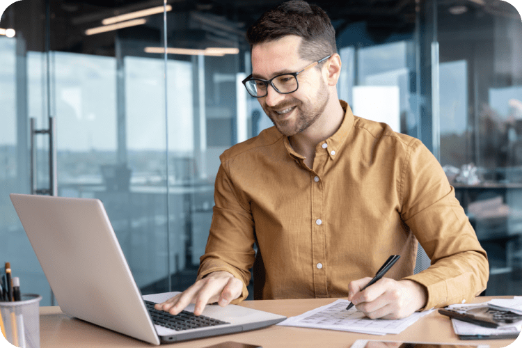 A man in a yellow shirt and glasses works on his computer at the office