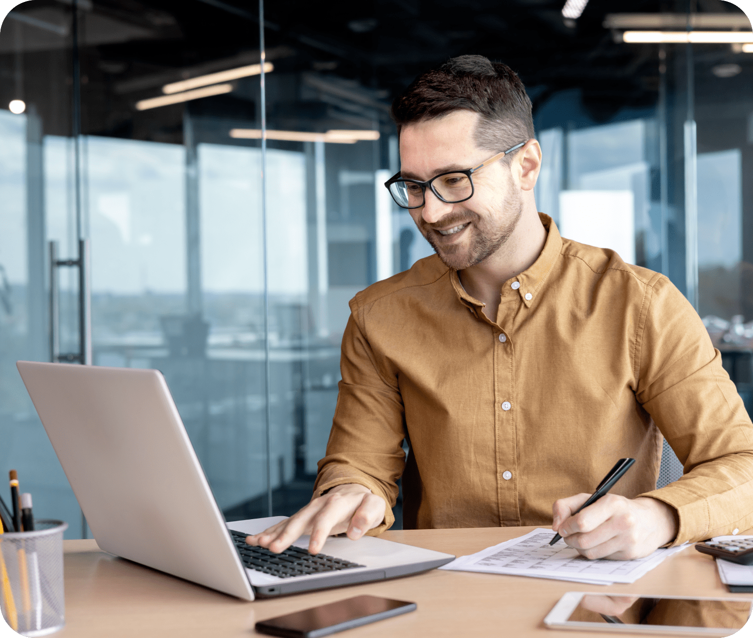 A man in a yellow shirt and glasses works on his computer at the office