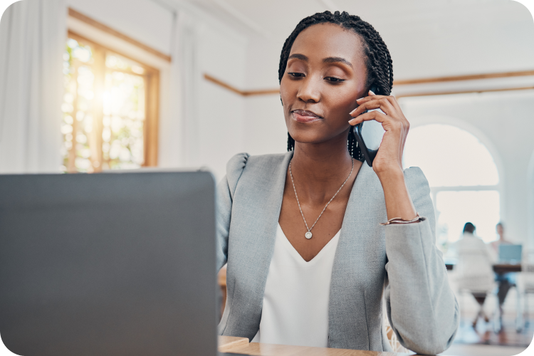 A woman in a grey blazer speaks on the phone at her desk in the office