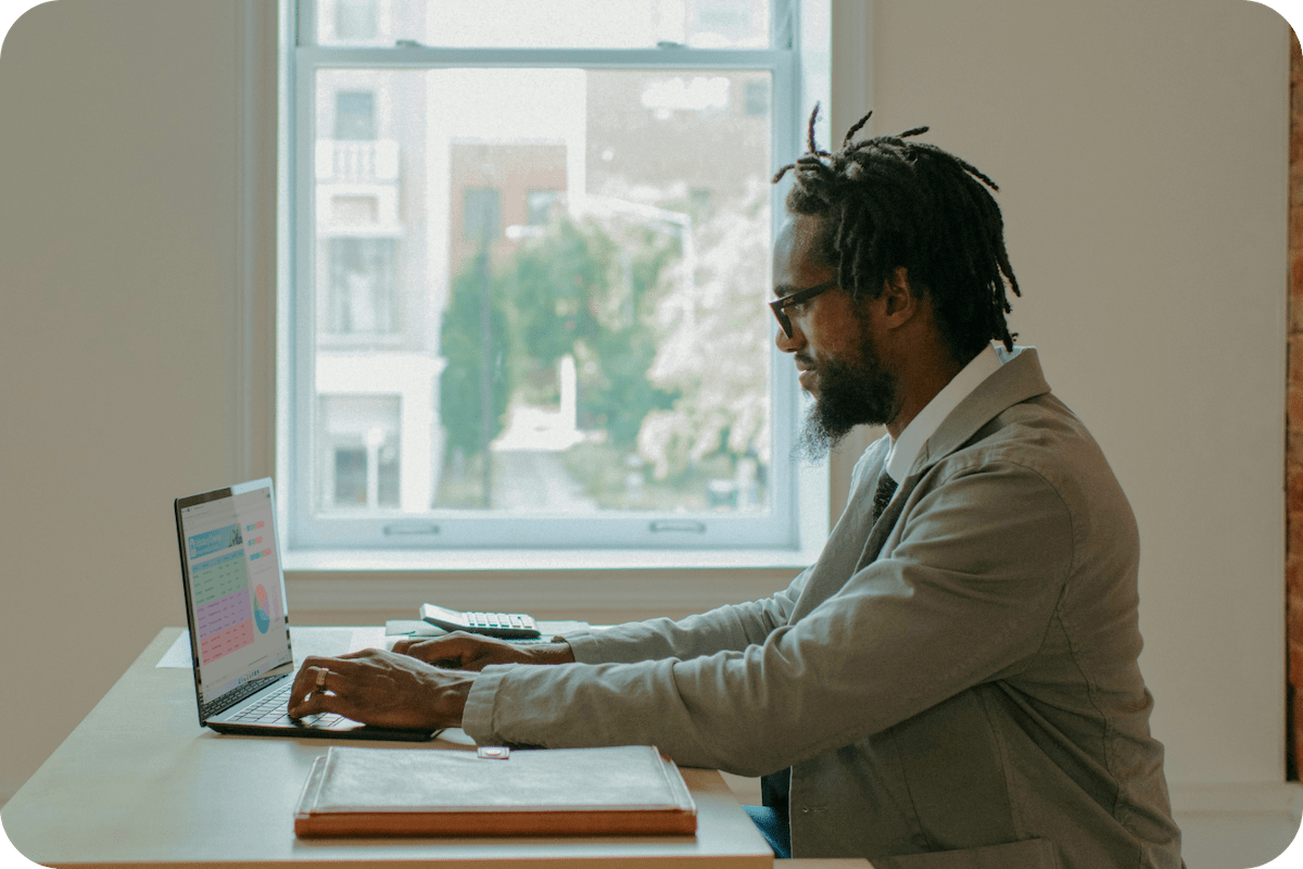 Man sits at his desk working on a computer in front of a pretty city view